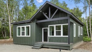 Eine zweigeschossige Holzhütte mit Veranda, großen Fenstern und einem geneigten Dach.