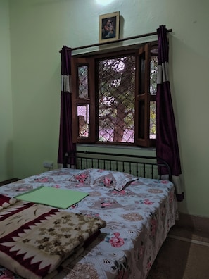 Ein Schlafzimmer mit einem Bett, einem Fenster mit Vorhängen, einem Bild an der Wand und einem grünen Gegenstand auf dem Bett.
