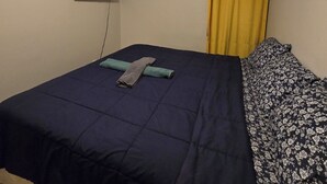 Un dormitorio con una cama, un televisor de pantalla plana en la pared y una cortina amarilla.