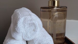 Uma garrafa de vidro transparente com um dispensador dourado, uma toalha branca e um tabuleiro de madeira.