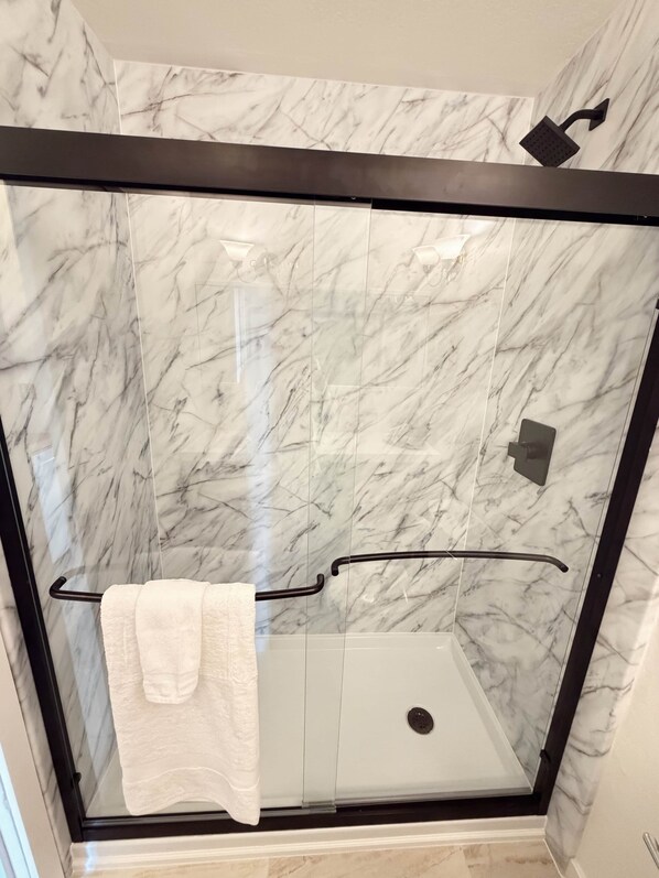 A glass-enclosed shower with a marble wall, a towel rack, and a shower control panel.
