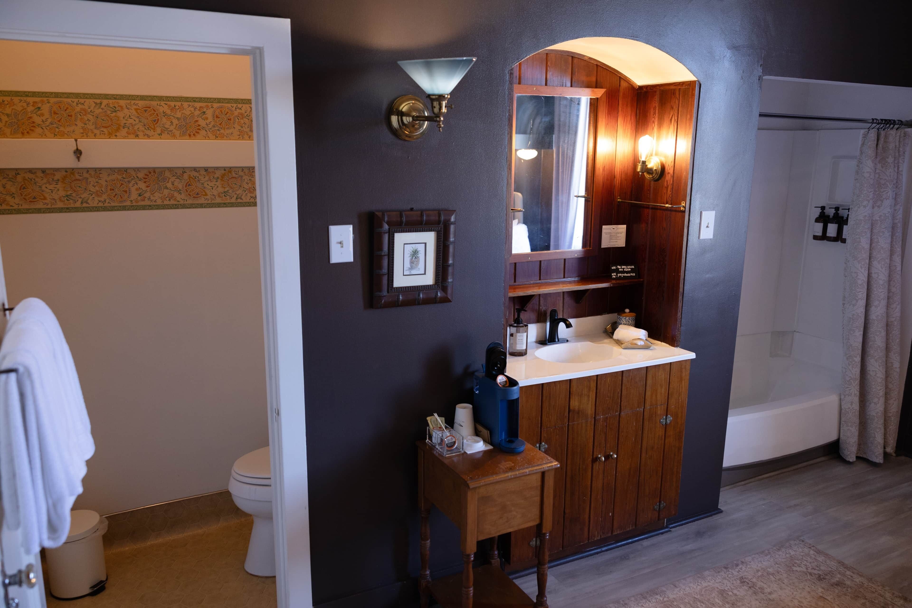 A bathroom with a wooden vanity, a mirror, a toilet, and a shower area.