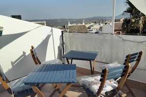 A balcony with two blue chairs and a small table, overlooking a cityscape with buildings and a mountain in the distance. - Roof Terrace - Pet - WiFi - Parking - Sleeps 4 (Rute)