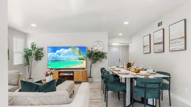 A modern living room with a flat-screen TV, a dining area with a white table and green chairs, and a hallway with a door. - Ranch-Style w Gated Yard, 4 Parking, 4 Bedroom 3 Bathroom (La Mesa)