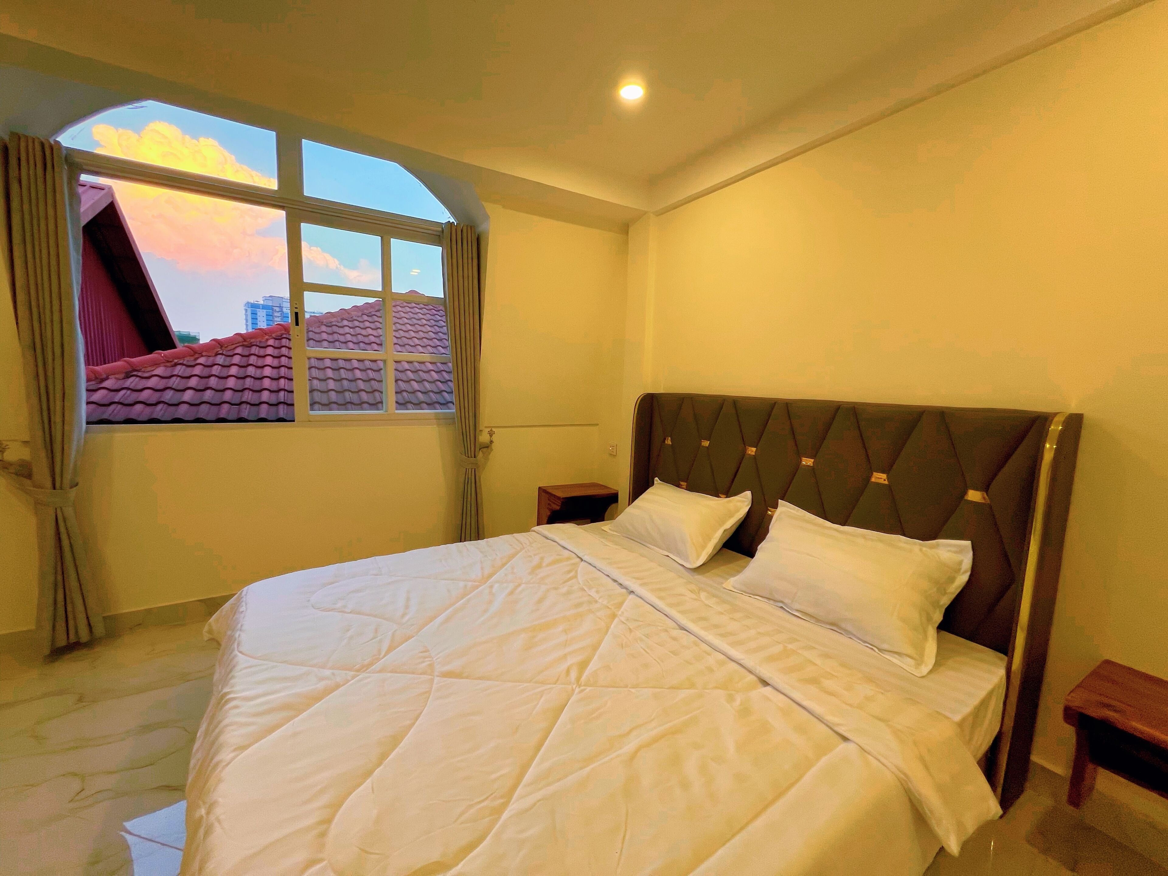 A bedroom with a bed, a window, a nightstand, and a view of buildings.