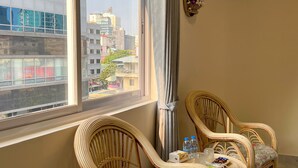 A room with a large window, two wicker chairs, a small table with water bottles and snacks, and a mirror on the wall. - A Z Hotel Phnom Penh (Phnom Penh)