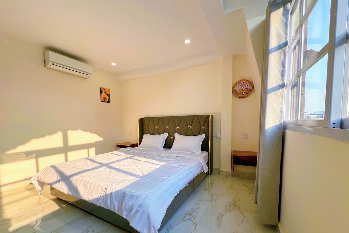 Una cama bien hecha en una habitación con suelo de mármol, aire acondicionado de pared y ventana con vistas.