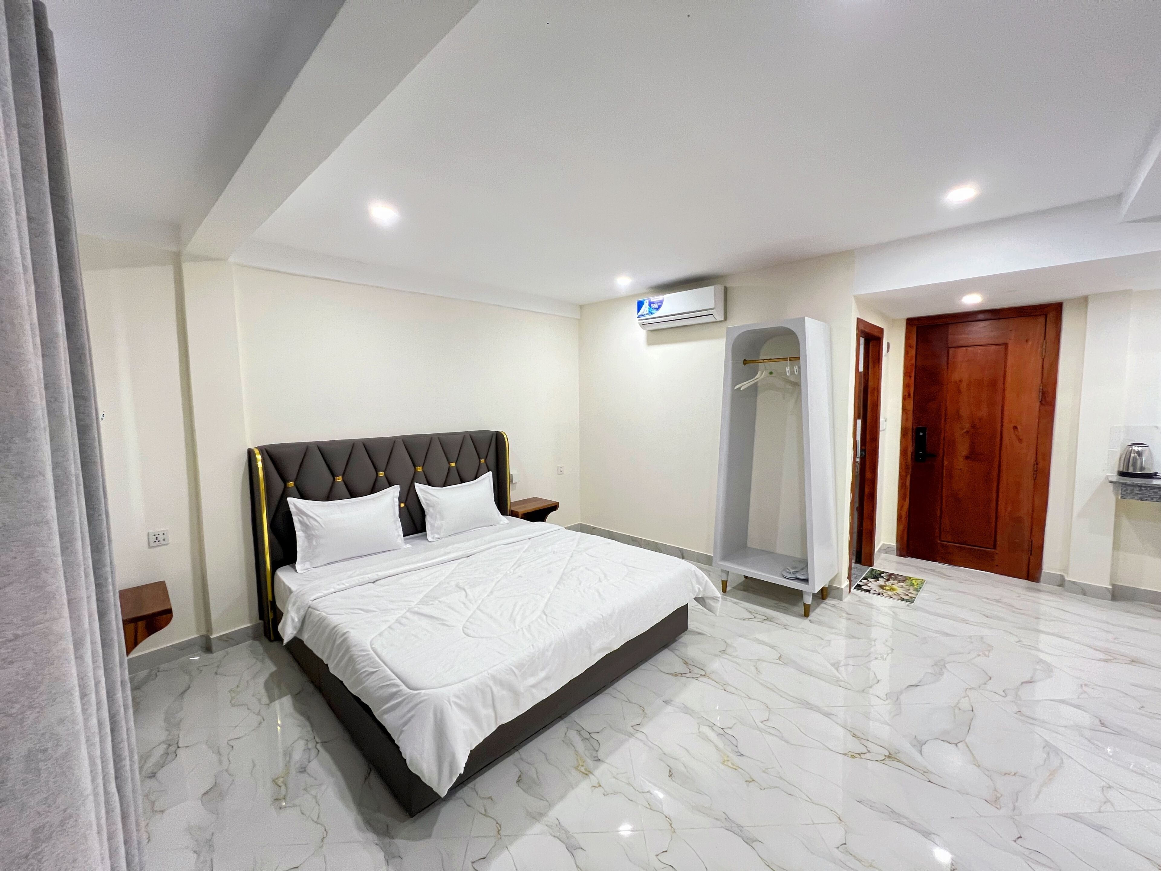 A hotel room with a bed, a walk-in closet, a wooden door, and a marble floor.