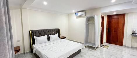 A hotel room with a bed, a walk-in closet, a wooden door, and a marble floor.