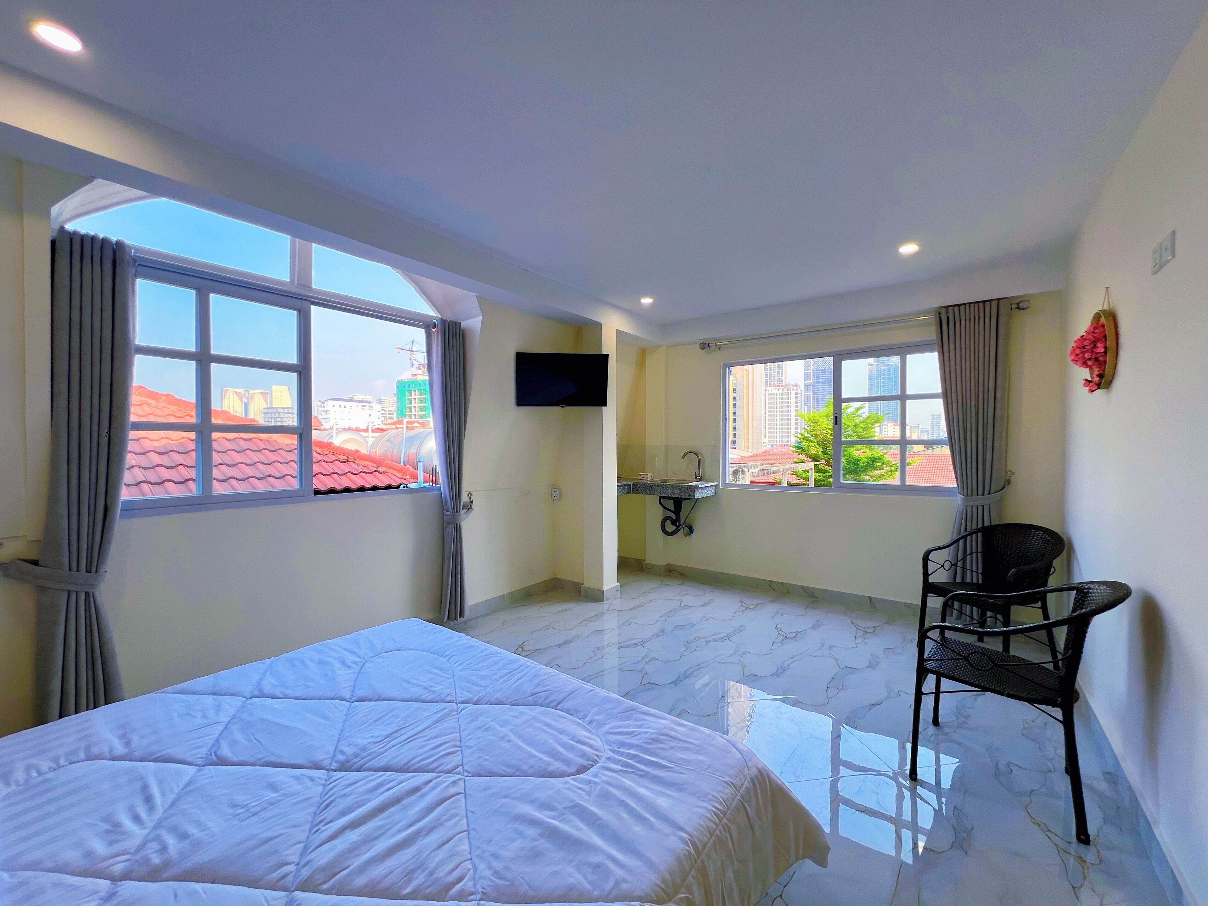 Habitación de hotel con cama, televisión, silla y ventana con vista a edificios.
