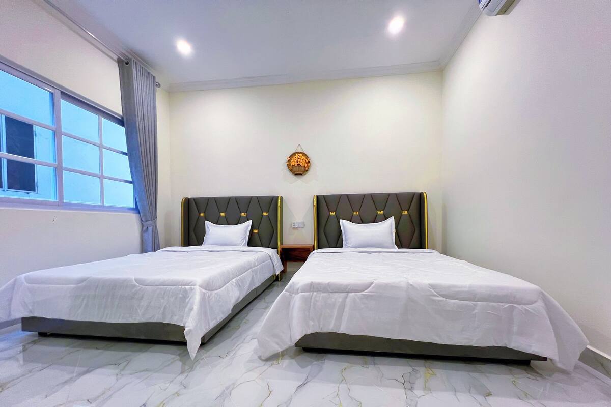 Una habitación de hotel con dos camas, piso de mármol, una ventana con cortinas y un reloj de pared.