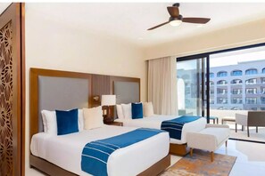 Ein Hotelzimmer mit zwei Betten, einem Deckenventilator, einem großen Fenster und Blick auf ein Gebäude.