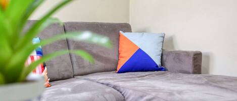 A grey sofa with a blue and orange pillow, a white table, and a green plant.