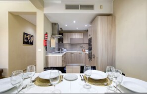 A dining area with a table set for four, a kitchen in the background, and a fire extinguisher on the wall. - Marsaskala Escape Pool Beaches Local Charm (Marsaskala)