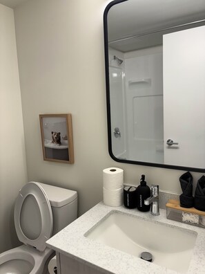 A bathroom with a toilet, sink, mirror, and a framed picture on the wall. - Smart Studio Stay | Work + Relax (Edmonton)