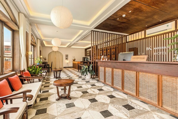 Un espace d’accueil d’hôtel comprenant un comptoir d’enregistrement, des sièges et un sol à carreaux.