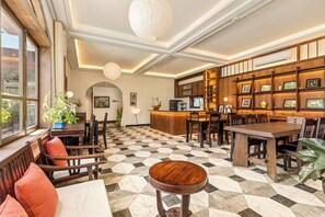 Un hall d’hôtel avec un sol à carreaux, des meubles en bois, un comptoir d’accueil et un mur orné de tableaux.
