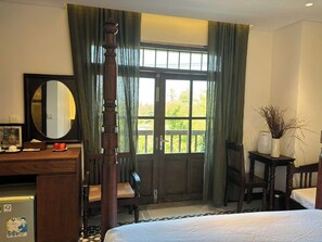 Una camera d'albergo con un letto, una scrivania con uno specchio, una sedia, un tavolino con un vaso e una finestra con tende.