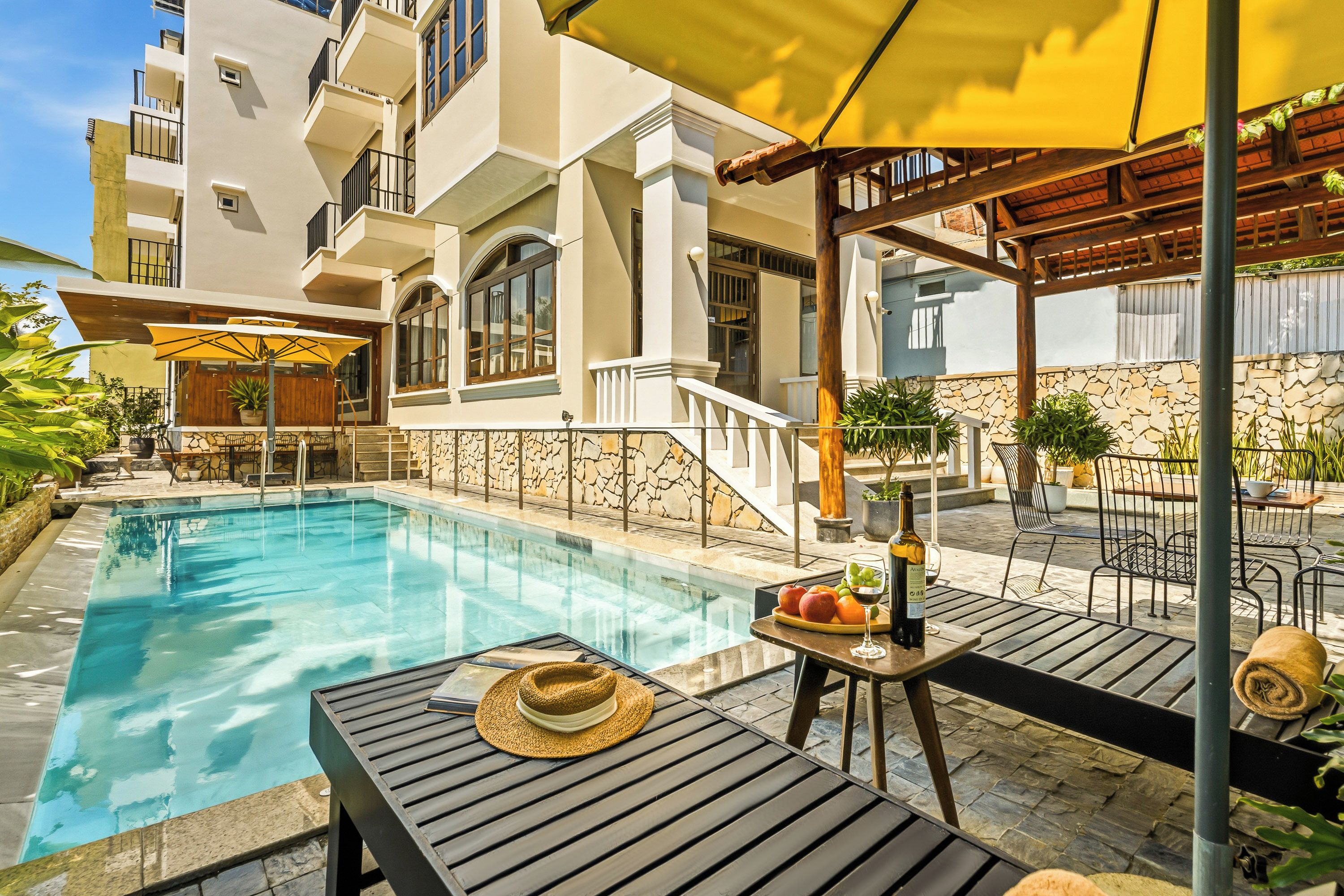 Una piscina con muelle de madera, mobiliario exterior y un muro de piedra.