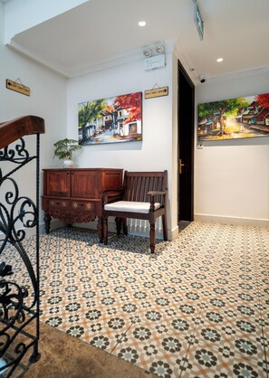 Une pièce avec des carreaux de sol à motifs, un banc en bois, une armoire et deux tableaux accrochés aux murs.