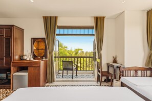 A hotel room with a balcony, a desk, a chair, a bed, and a small table. - Manterra Hoi An Hotel (Da Nang)