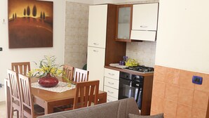 Ein Wohnzimmer mit einer Couch, einem Esstisch mit Stühlen, einer Küchenzeile mit Schränken und Geräten sowie einem Bild an der Wand.