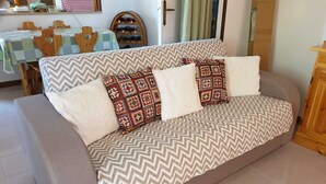 A sofa with patterned cushions, a dining table with chairs, and a wine rack in a room with a door and curtains. - Villa Marisol with parking space and large garden (San Pietro In Bevagna)