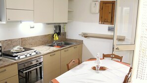 A kitchen with a stove, sink, and cabinets, a dining table with chairs, and a window with curtains. - Villa with sea view in San Gregorio - Patu (Patu')