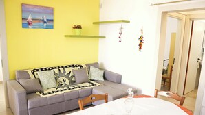 A living room with a sofa, a dining table, and a door leading to another room. - Villa with sea view in San Gregorio - Patu (Patu')
