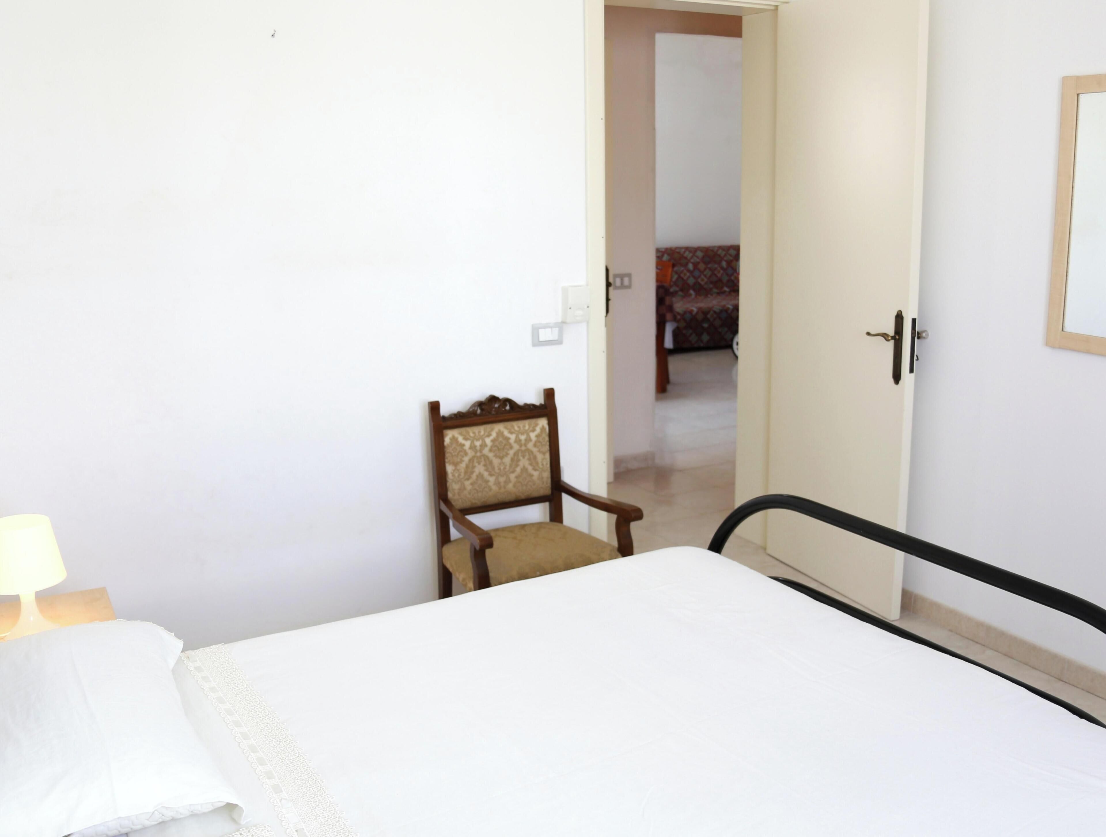 Ein Hotelzimmer mit einem Bett, einem Sessel, einem Nachttisch und einer Tür zu einem weiteren Raum.