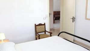 Ein Hotelzimmer mit einem Bett, einem Sessel, einem Nachttisch und einer Tür zu einem weiteren Raum.