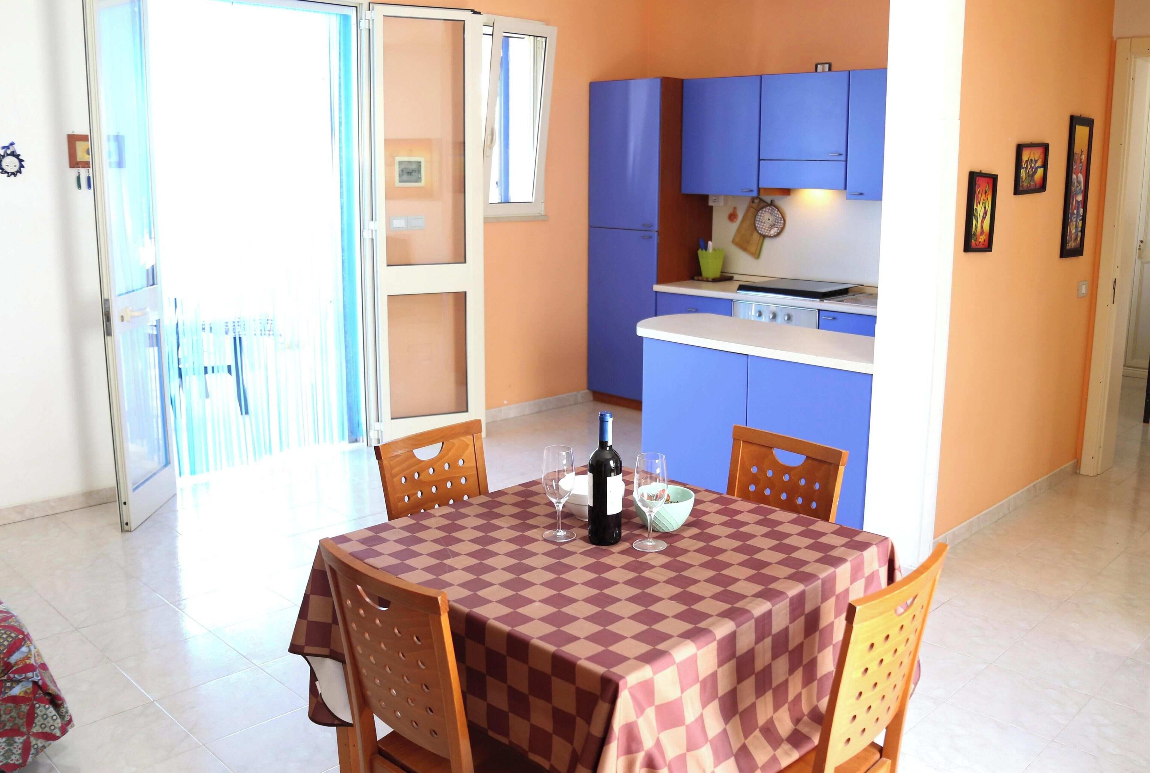 A dining area with a checkered tablecloth, wooden chairs, a bottle of wine, and glasses.