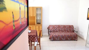 Ein Zimmer mit kariertem Tisch, einer gemusterten Couch, einem Holzschrank und einem Fliesenboden.