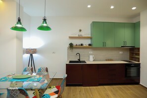 Eine moderne Küche mit grünen Schränken, einem eingebauten Backofen und einem Essbereich mit einem Glastisch und gemusterten Stühlen.