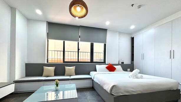 A modern hotel room with a bed, a seating area, a glass coffee table, and a large window. - Nghe Home (Da Nang)