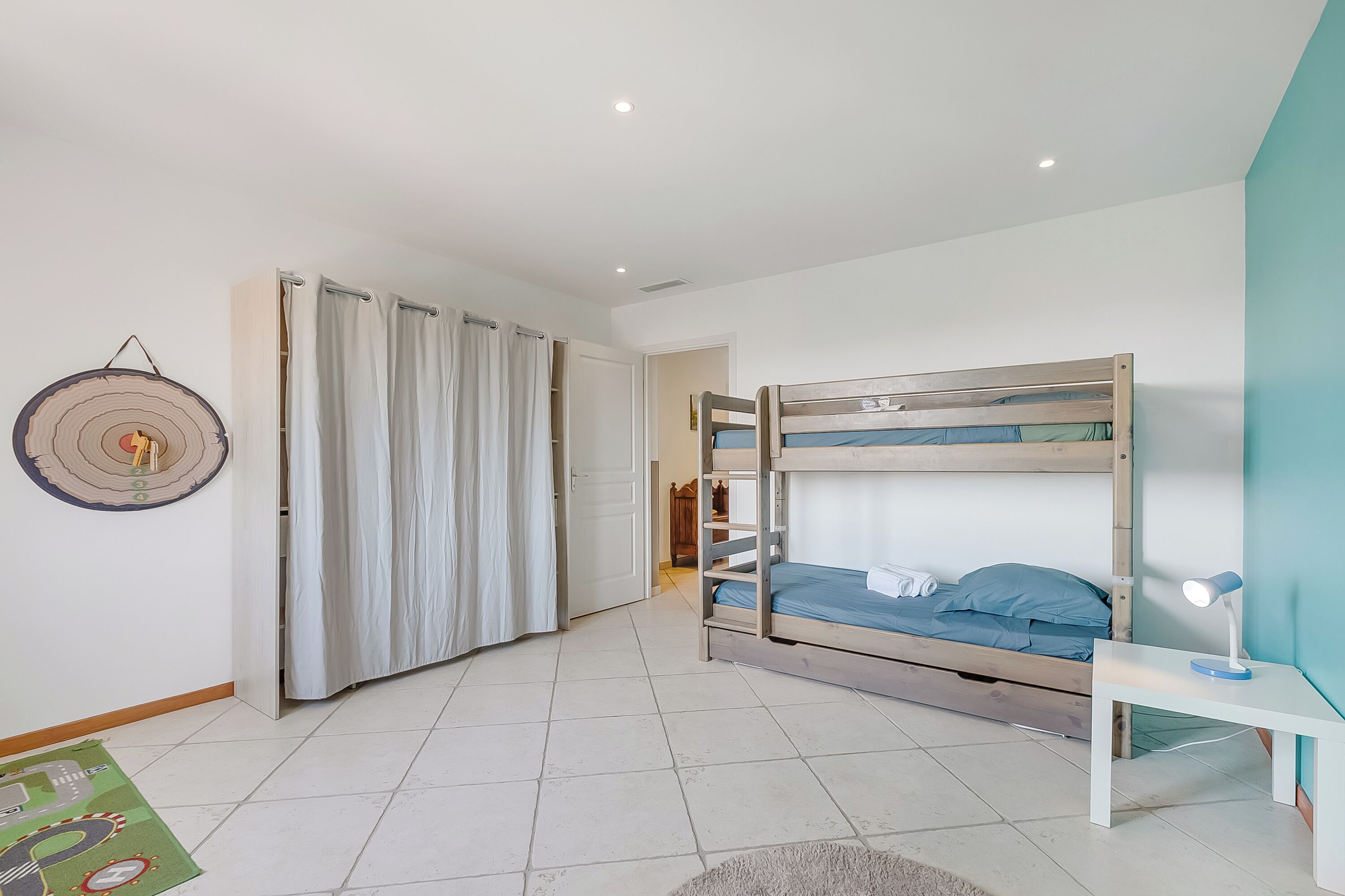 Une chambre avec des lits superposés, une table de chevet avec une lampe, un rideau et un élément de décoration murale.