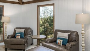 Ein Zimmer mit hohen Decken, Holzbalken, zwei Ledersessel mit Kissen, einem kleinen runden Tisch, einem Korbwannen und einer Lampe.