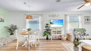 A modern living room with a dining area, a television, and a ceiling fan. - Beach in 90 Seconds w/ Hot Tub, Coffee Bar & Games (Indian Rocks Beach)