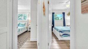 A hallway leading to two bedrooms with a bed, a nightstand, a lamp, and a window with curtains. - Beach in 90 Seconds w/ Hot Tub, Coffee Bar & Games (Indian Rocks Beach)