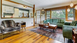 Una sala de estar con un sofá, sillón, mesa de centro y vista a la cocina por un ventanal amplio.
