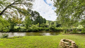 Un espacio cubierto de césped con un río, árboles y una estructura de piedra.