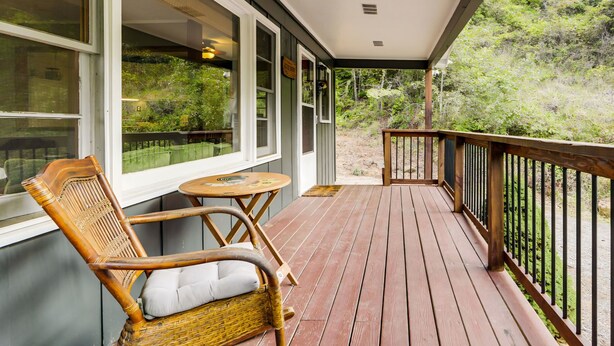Una terraza de madera con una mecedora y una pequeña mesa, con vista a un paisaje verde exuberante.