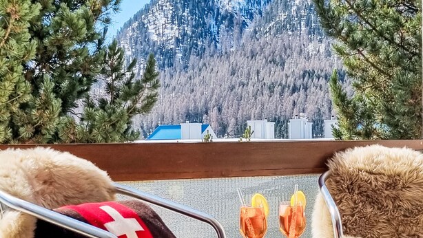A view from a window with a wooden table, two chairs, and two glasses of a beverage with lemon slices. - Chesa Piz Alv - Roseg Spirit by Interhome (Pontresina)