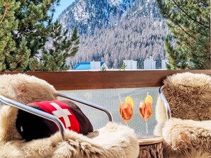 A view from a window with a wooden table, two chairs, and two glasses of a beverage with lemon slices. - Chesa Piz Alv by Interhome (Pontresina)