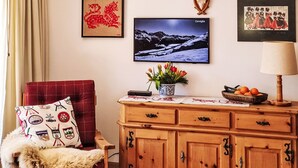A cozy living room with a red chair, a wooden cabinet, a television, and wall art including a mountain landscape and a red dragon. - Chesa Piz Alv - Roseg Spirit by Interhome (Pontresina)