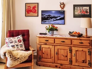 A cozy living room with a red chair, a wooden cabinet, a television, and wall art including a mountain landscape and a red dragon. - Chesa Piz Alv - Roseg Spirit by Interhome (Pontresina)