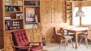 A cozy room with a red plaid chair, a wooden table with a pink tray, and a bookshelf filled with books. - Chesa Piz Alv - Roseg Spirit by Interhome (Pontresina)