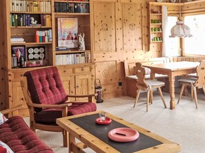 A cozy room with a red plaid chair, a wooden table with a pink tray, and a bookshelf filled with books. - Chesa Piz Alv - Roseg Spirit by Interhome (Pontresina)