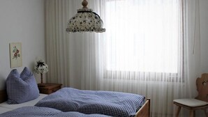 A bedroom with a bed, a chair, a nightstand, a hanging lamp, and a window with sheer curtains. - Chesa Piz Alv - Roseg Spirit by Interhome (Pontresina)