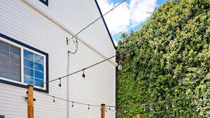 A patio with a table and chairs, a white building with windows, and a green ivy-covered wall.